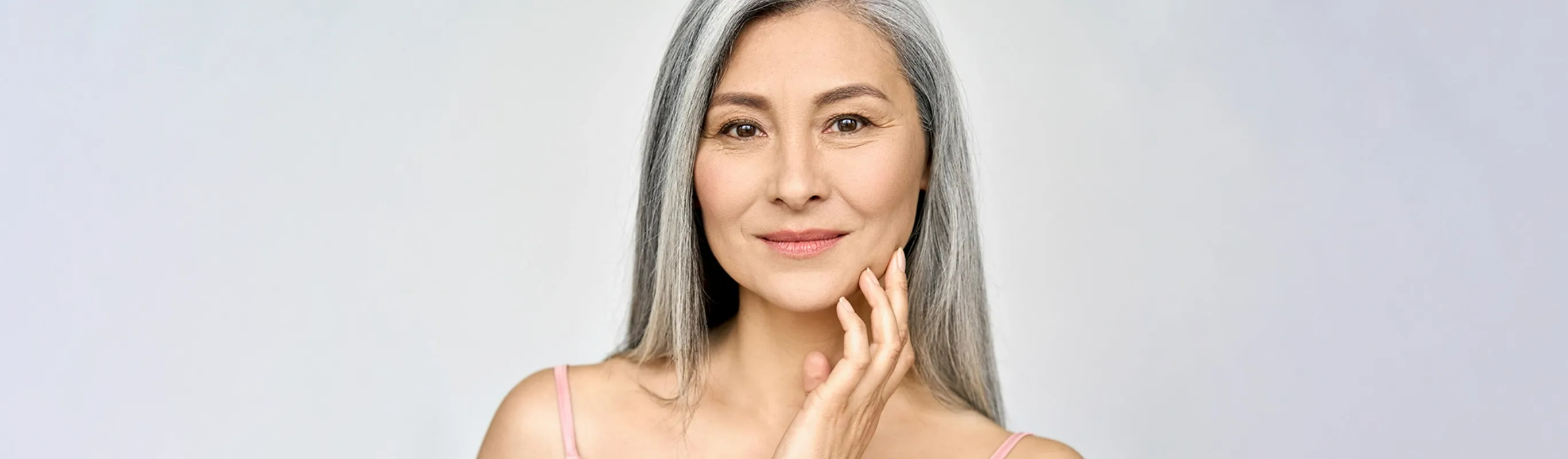 older woman with thin gray hair smirking with her hand grazing her cheek