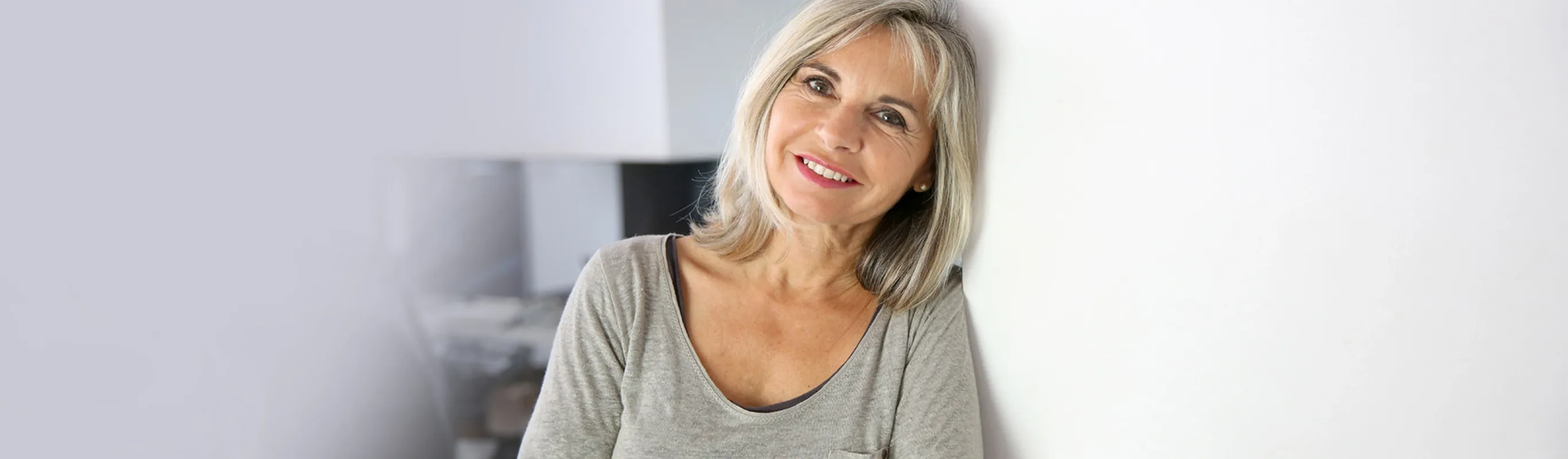 elder woman with short gray hair leaning against a wall smiling 