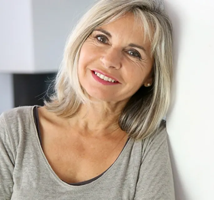 elder woman with short gray hair leaning against a wall smiling 