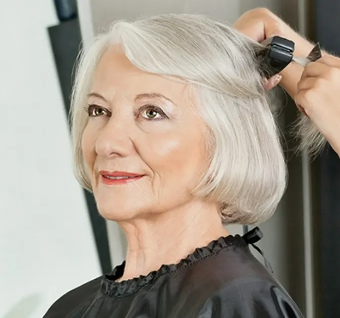 older woman getting her gray hair flat ironed at a salon by a hair stylist