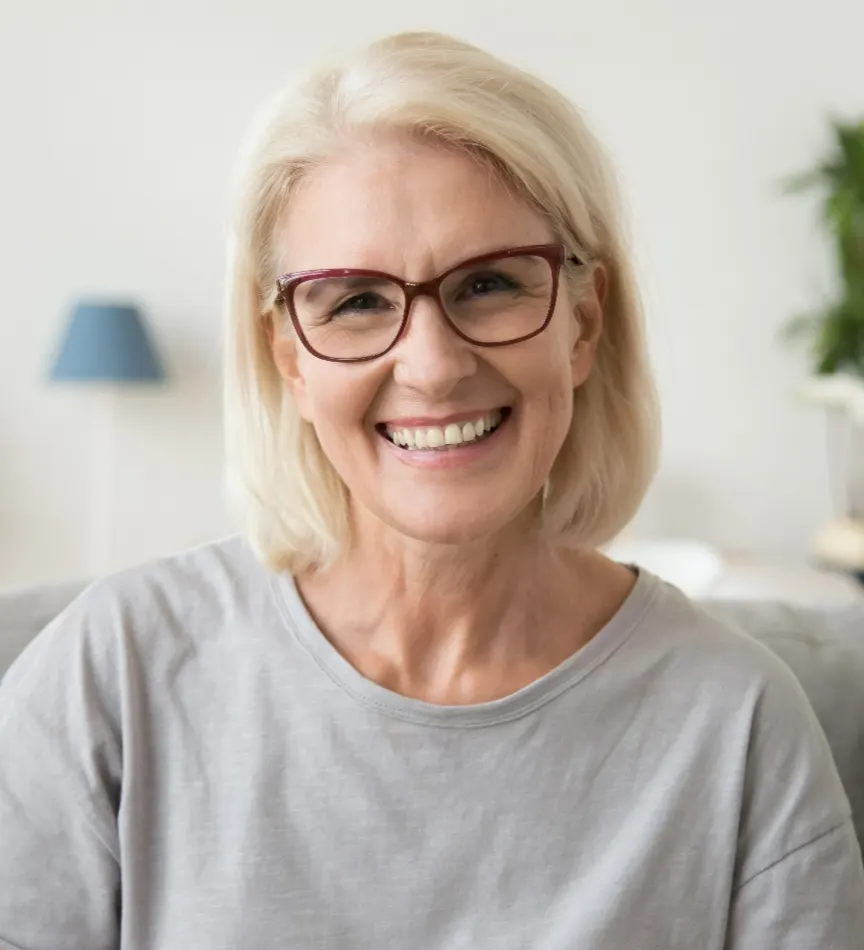 Smiling middle aged mature grey haired woman looking at camera while sitting on sofa in living room