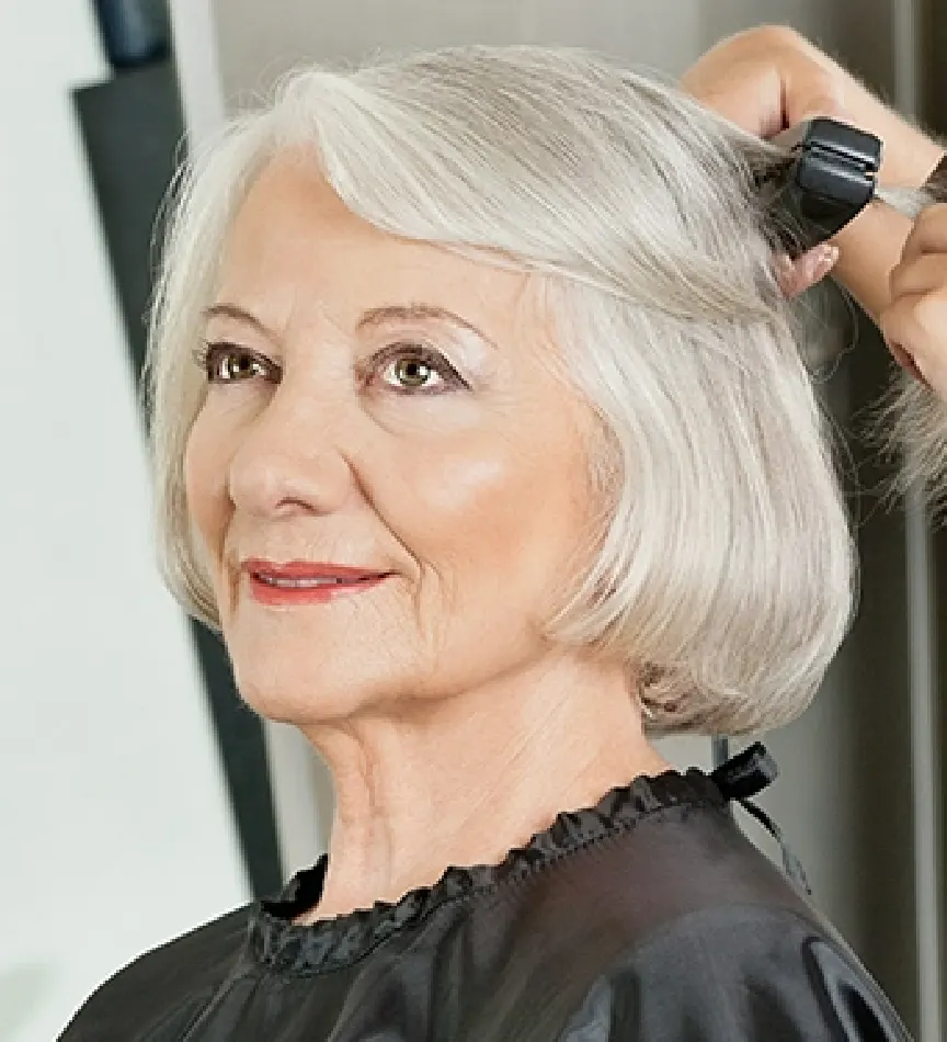 older woman getting her gray hair flat ironed at a salon by a hair stylist