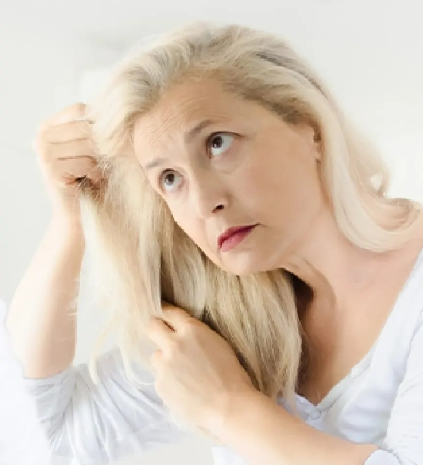 Upset senior woman looking through her thin hair as she stands in her bedroom looking in the mirror