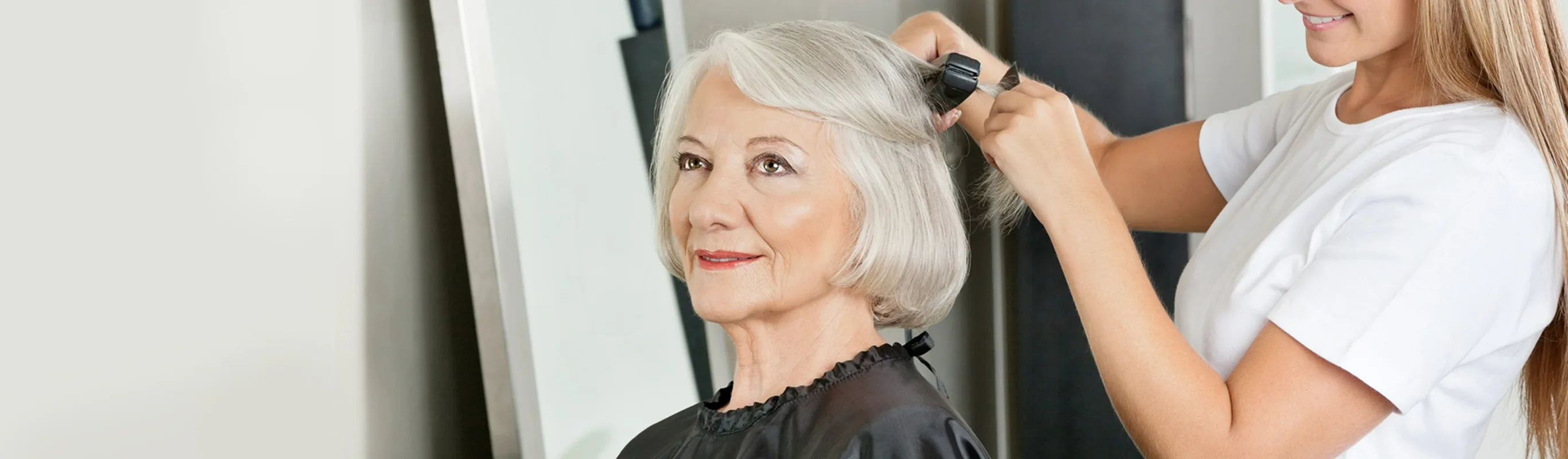 older woman getting her gray hair flat ironed at a salon by a hair stylist