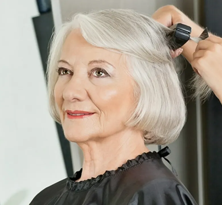 older woman getting her gray hair flat ironed at a salon by a hair stylist