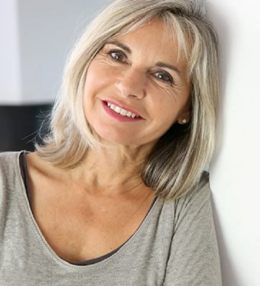 elder woman with short gray hair leaning against a wall smiling 