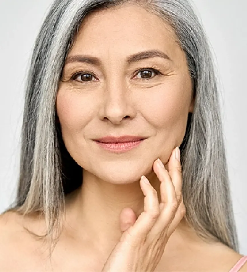 older woman with thin gray hair smirking with her hand grazing her cheek