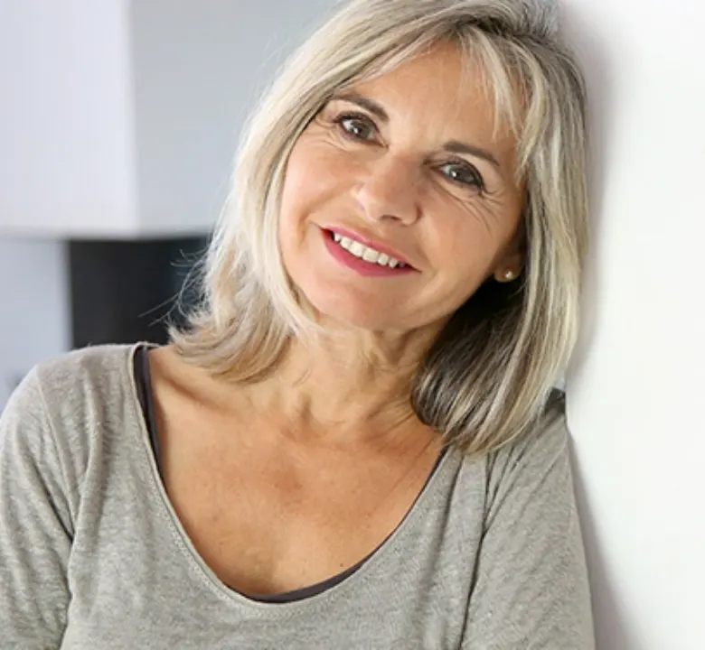 elder woman with short gray hair leaning against a wall smiling 