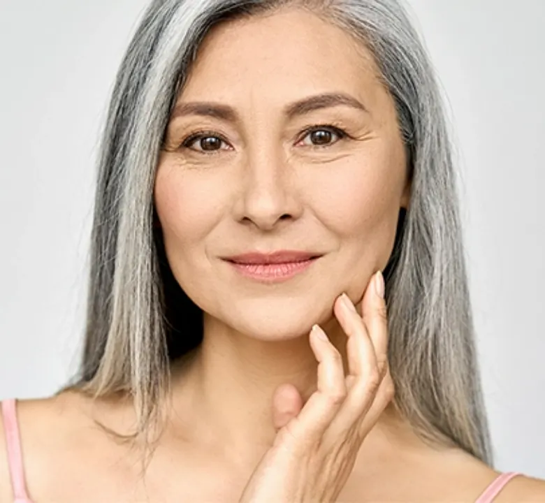 older woman with thin gray hair smirking with her hand grazing her cheek