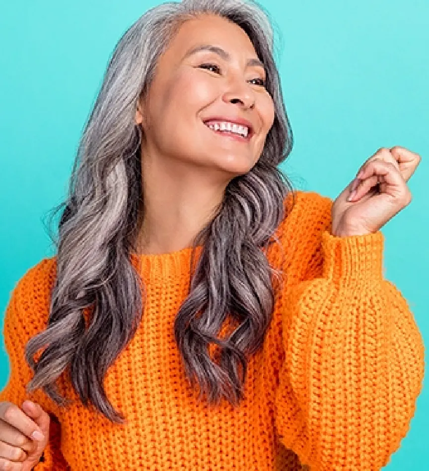 older woman with curly gray hair smiling and dancing wearing an orange sweater in front of a teal background