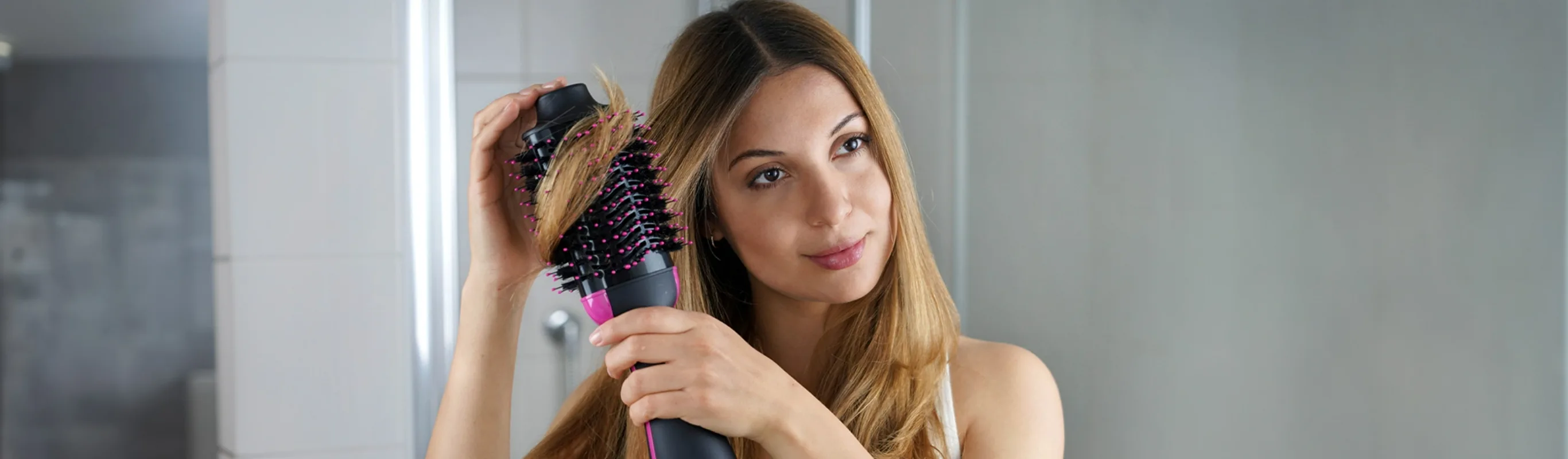 Girl using a brush hair dryer to style and diffuse her thinning hair while looking at herself in the bathroom mirror