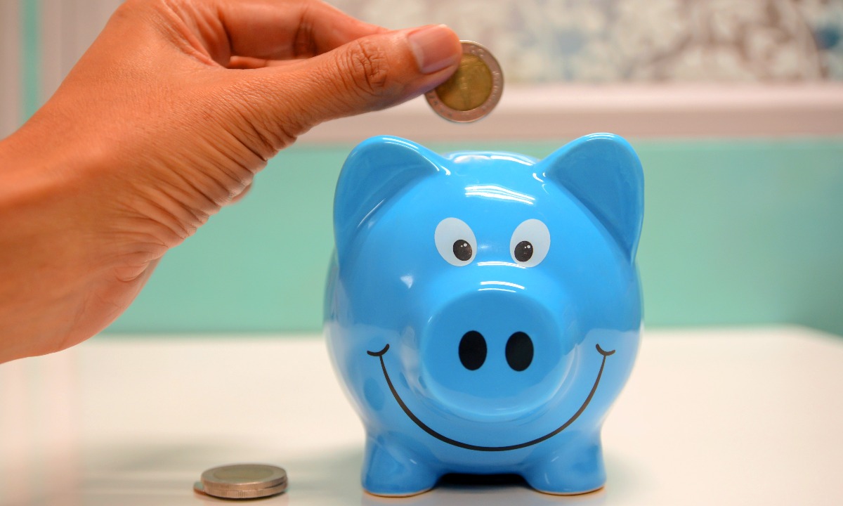 a hand holding a coin over a piggy bank