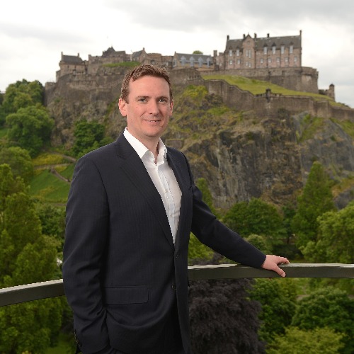 a man in a suit standing in front of a castle