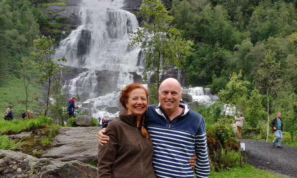 a man and woman posing for a picture in front of a waterfall