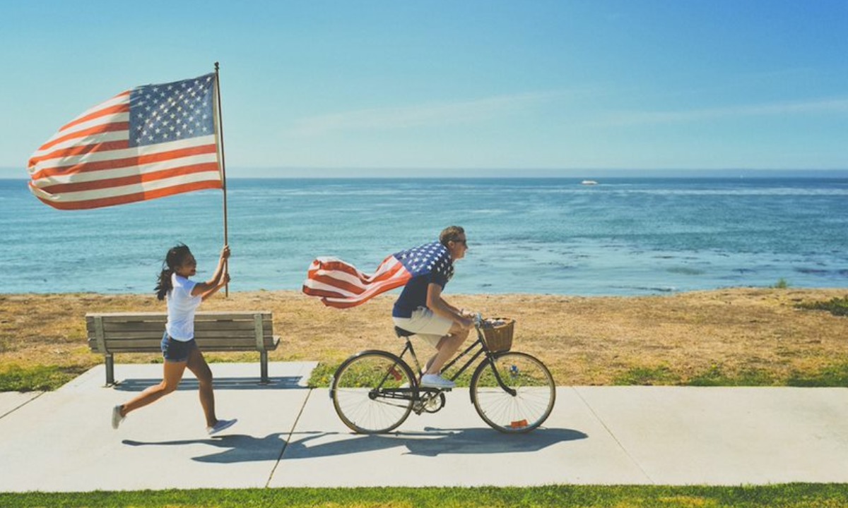 a man and woman riding a bicycle with a flag on the back
