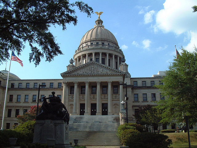 a large white building with a statue in front of it with Mississippi State Capitol in the background