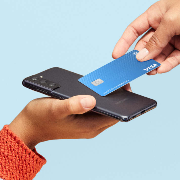 Close-up of two people, one holding a cell phone and the other holding a credit card to the cell phone to pay.