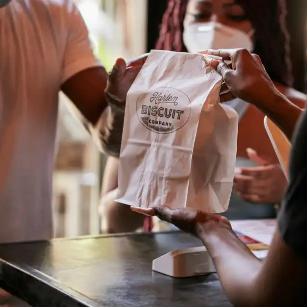 Empleado de Harlem Biscuit Company pasa bolsa de biscuits al cliente