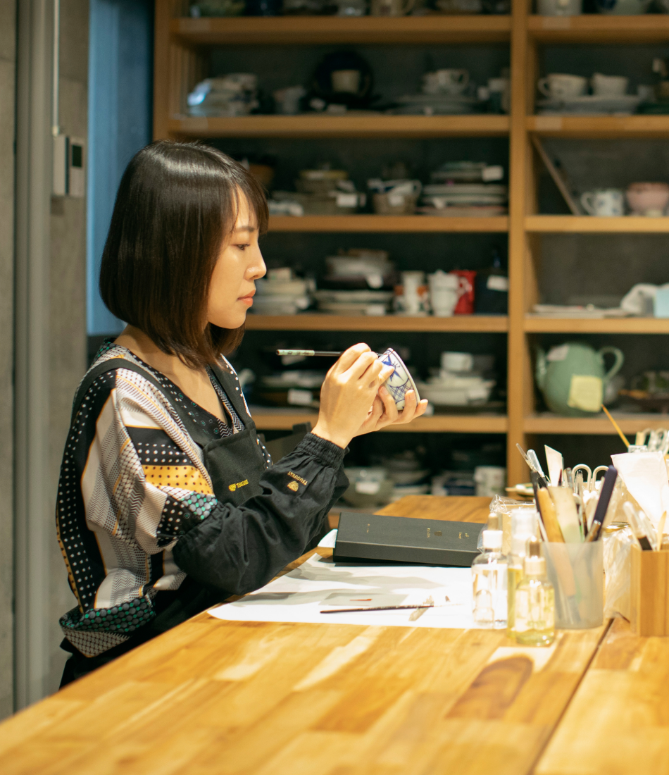 A person kneels on the ground looking at items for inventory in front of a wall with jars of loose-leaf herbs.