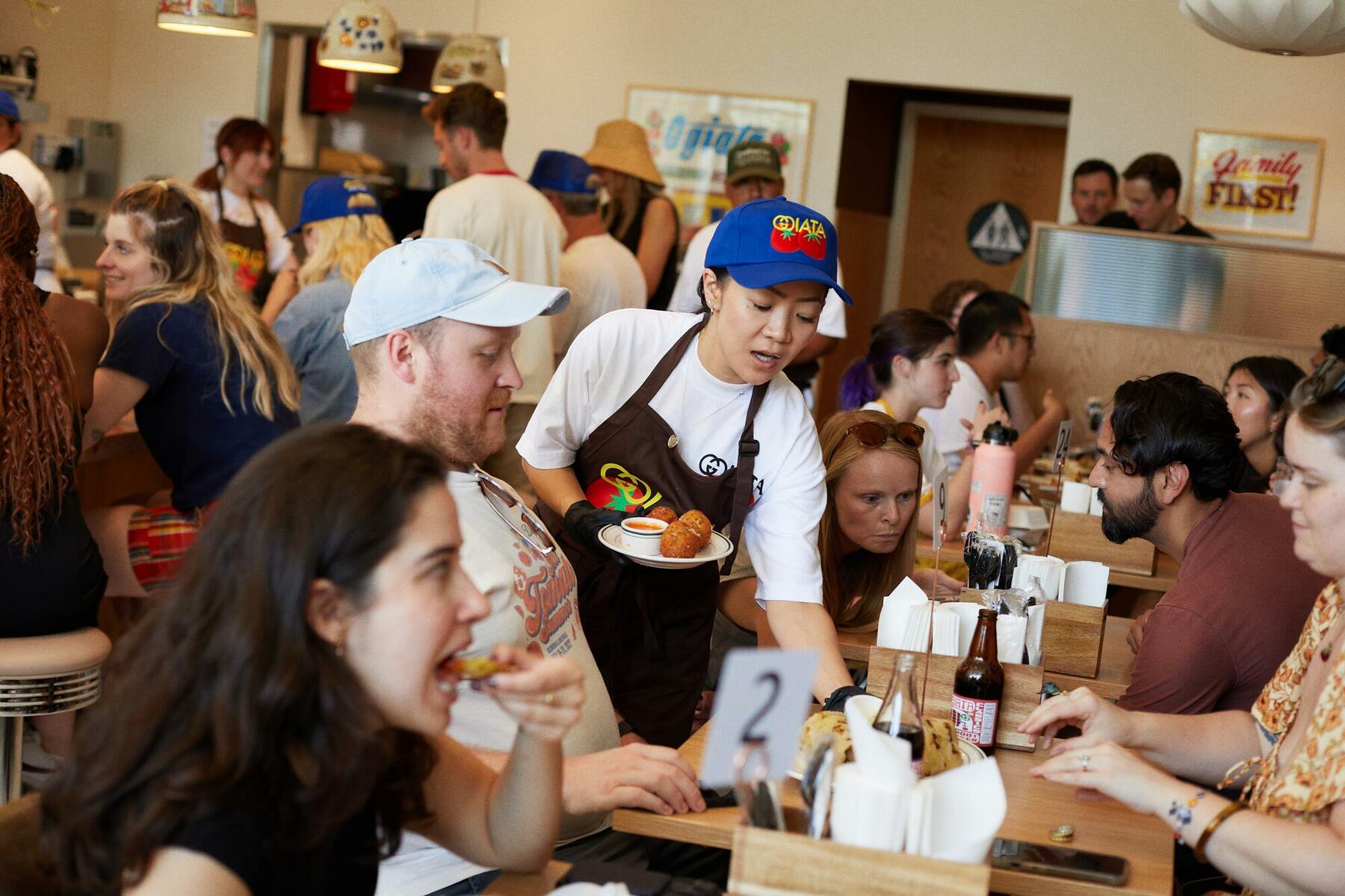 Server carrying a plate of food through a busy restaurant full of diners