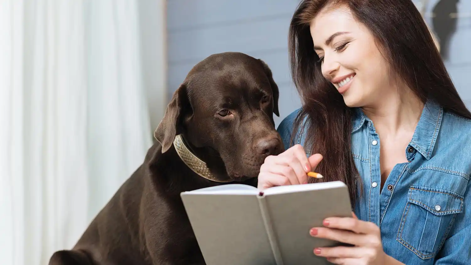 a woman writing a journal entry while her dog looks on, curious