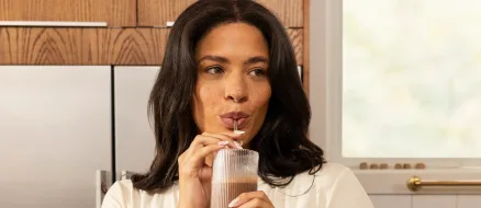 A woman sipping a drink in a kitchen