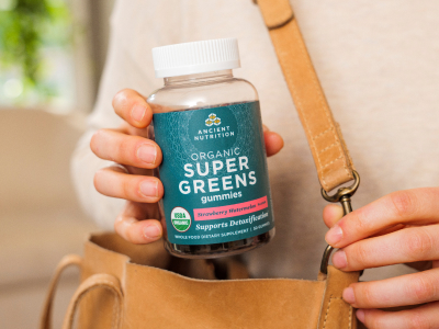 a person holding a bottle of supergreens gummies next to their purse