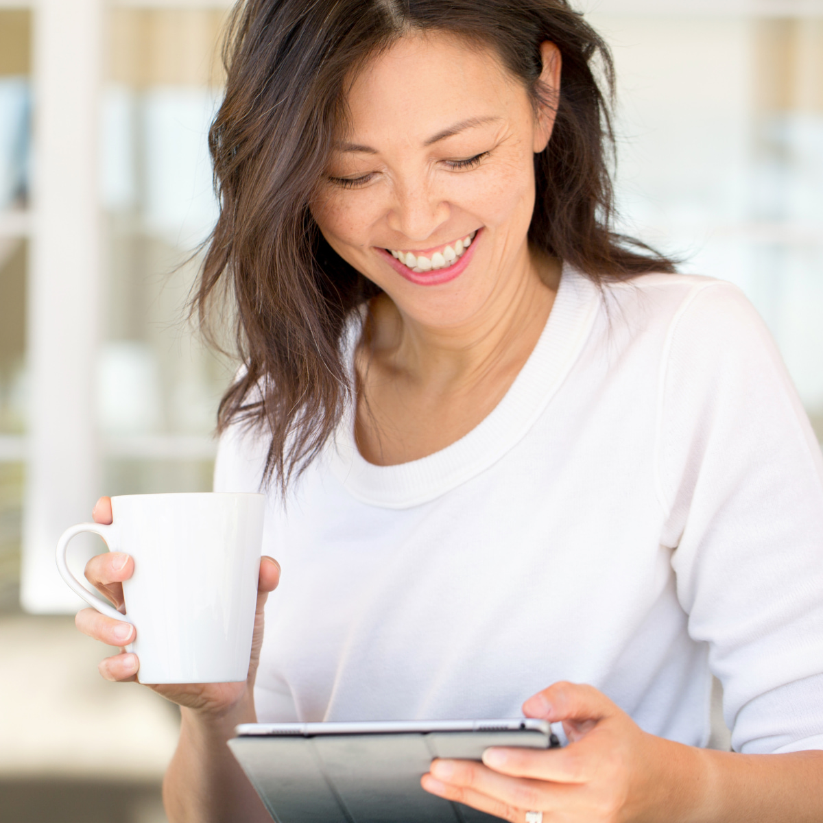 a woman holding a coffee cup looking at an ipad