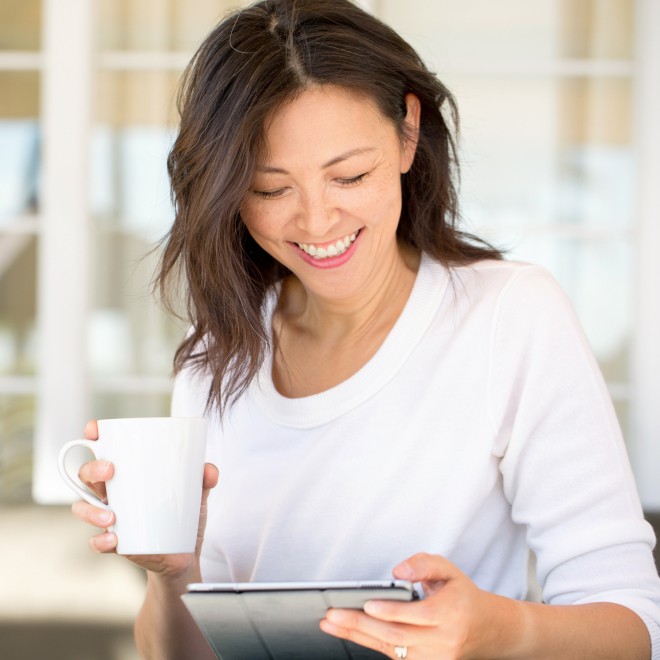 a woman holding a coffee cup looking at an ipad