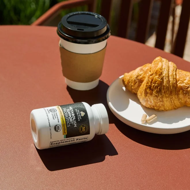 coffee cup, supplement bottle and a croissant on a table 
