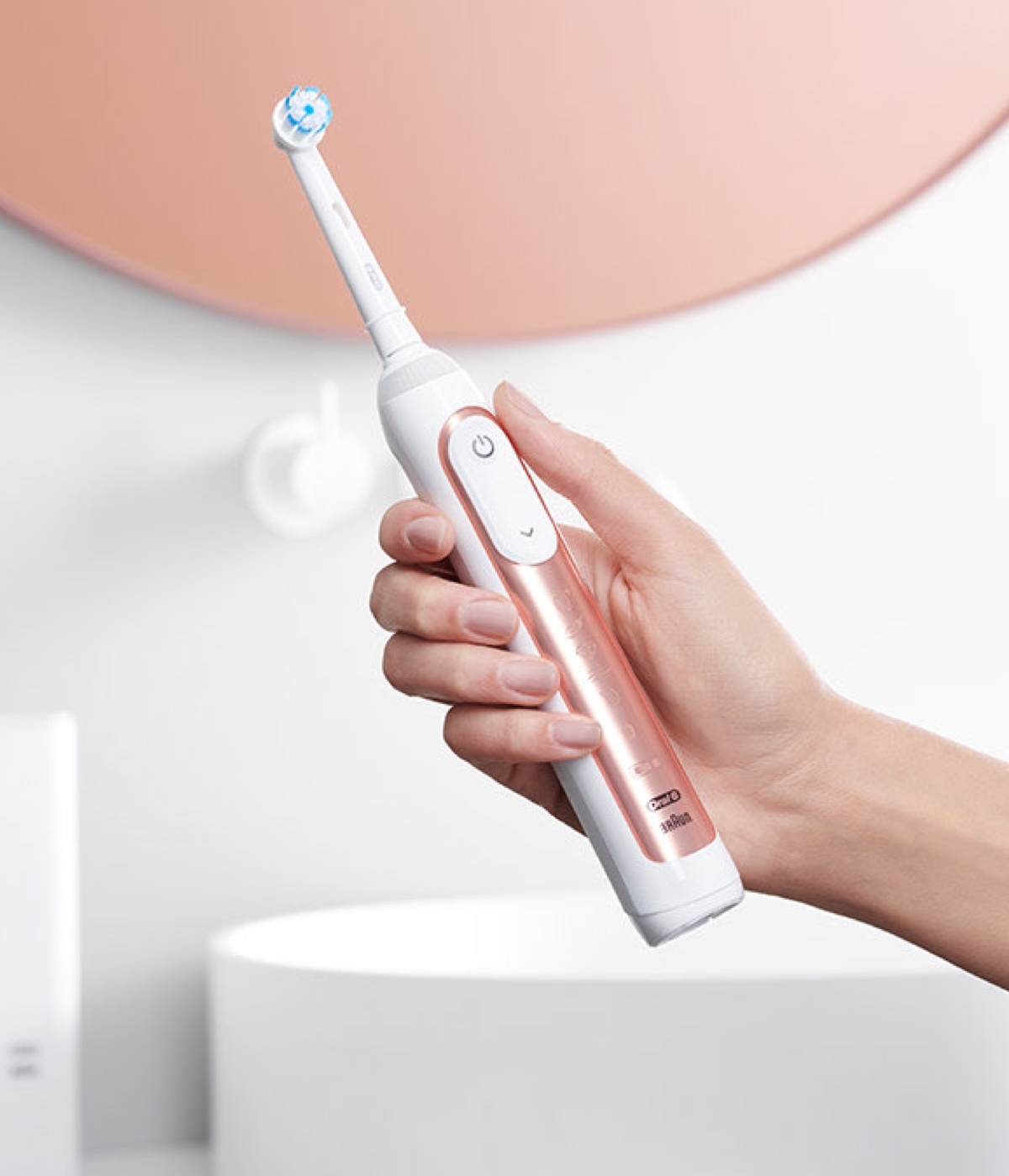 Mulher a segurar uma escova de dentes elétrica Oral-B Genius X em rosa dourado undefined