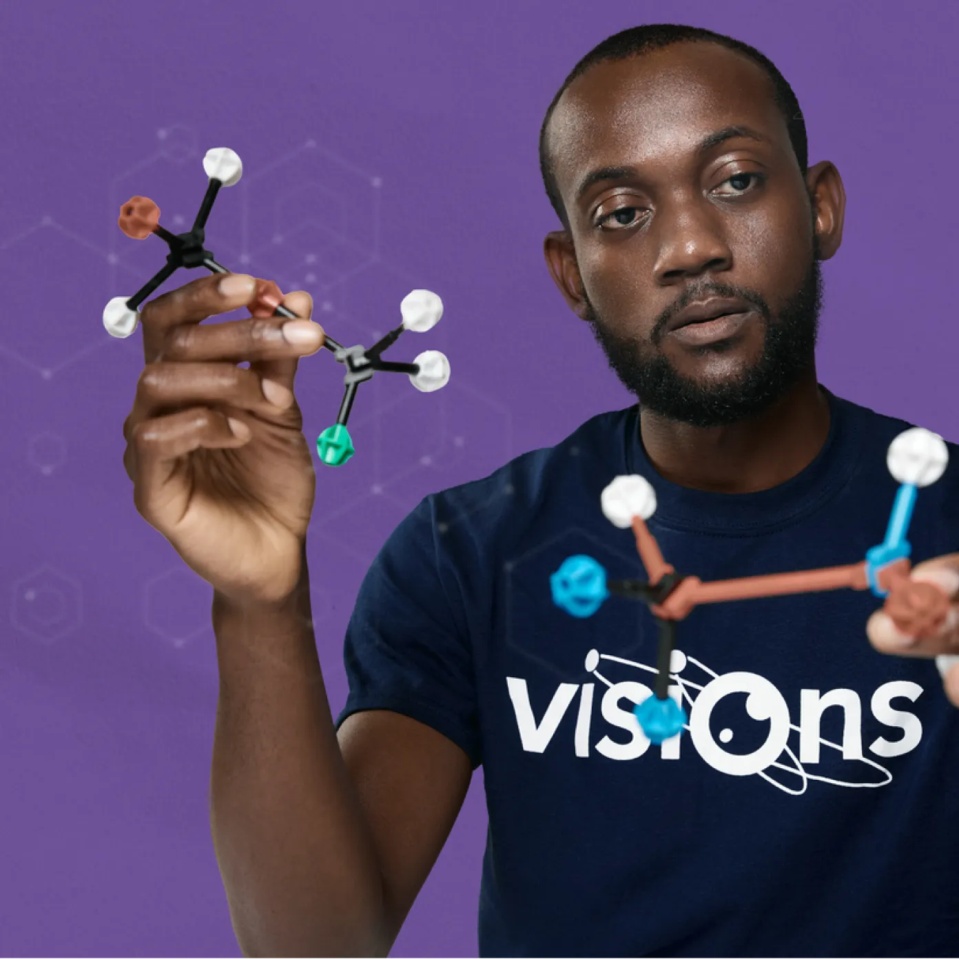 Person holding a molecular model against a purple background, wearing a Visions t-shirt.