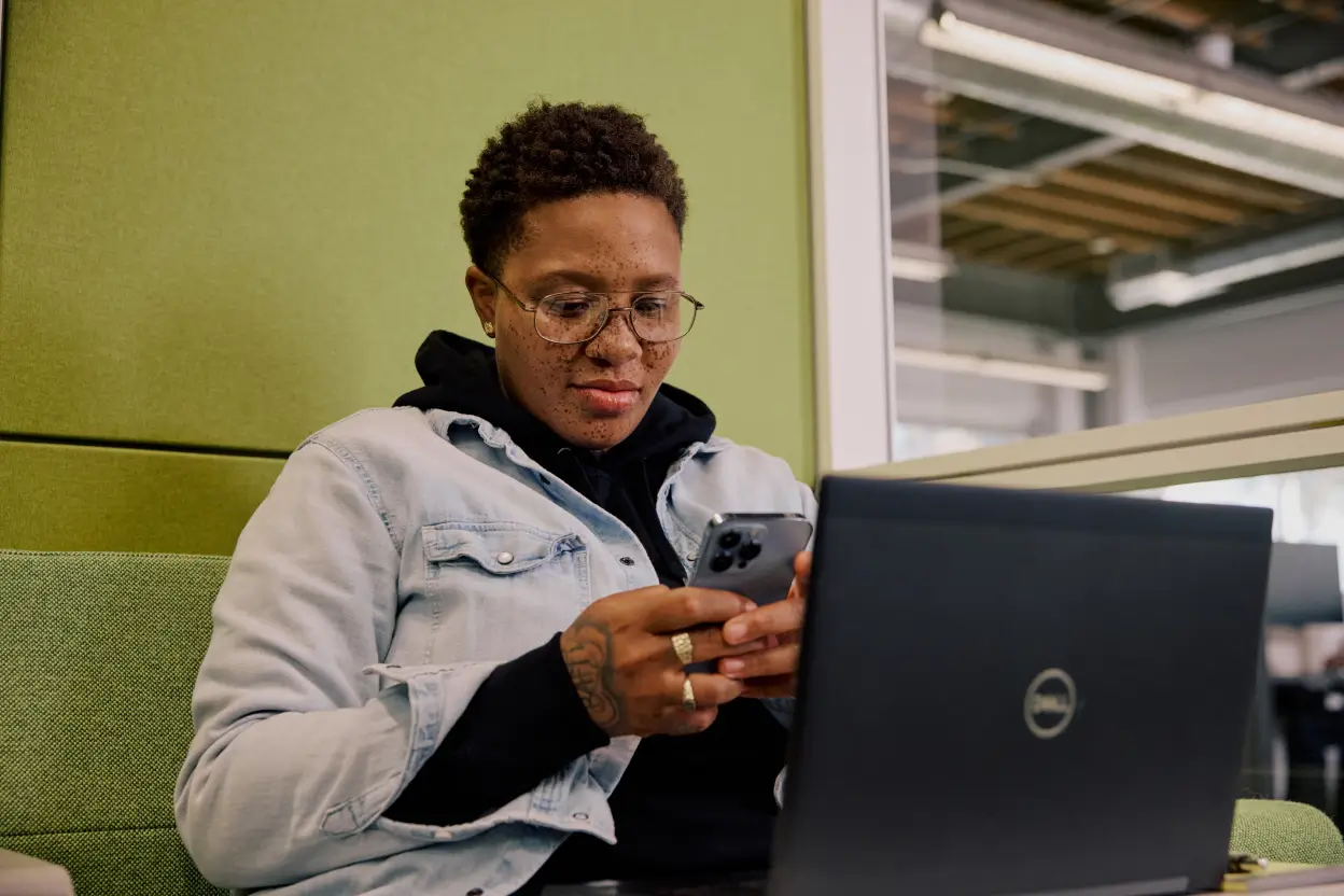 Person using 1Password’s password manager to securely log in from her mobile phone and laptop at the office.
