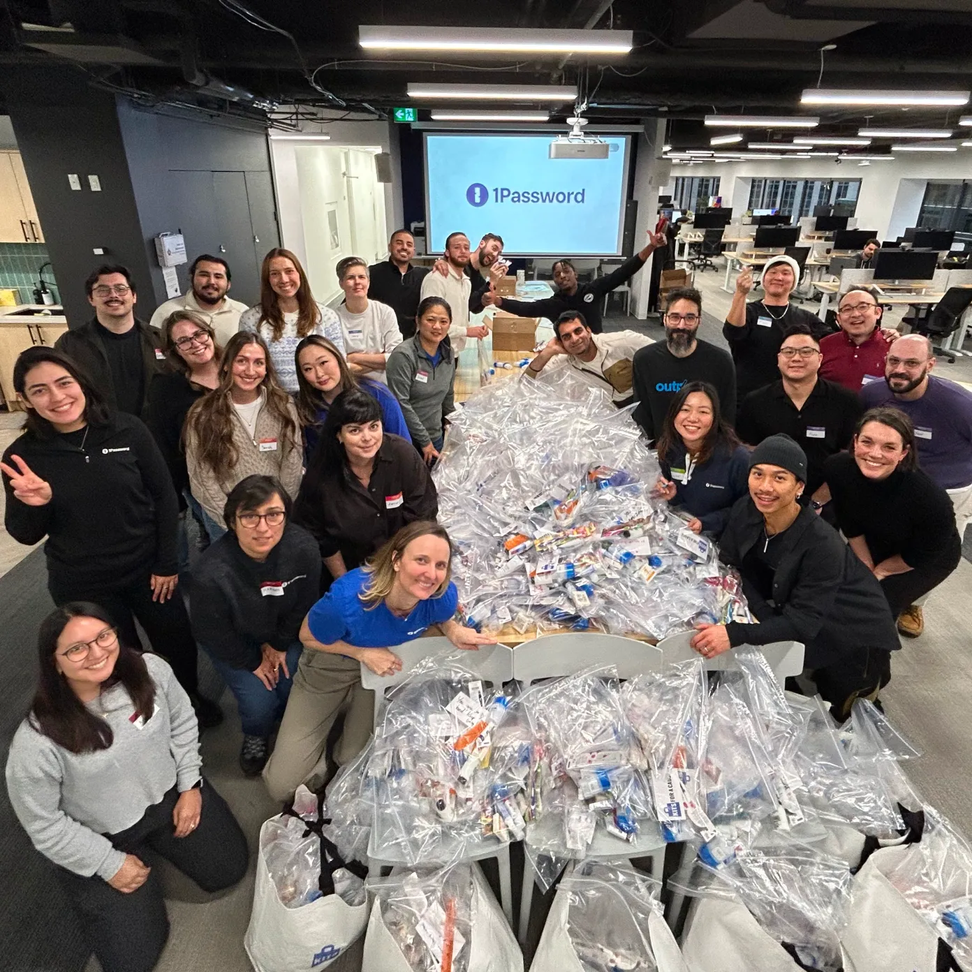 Large group of 1Password employees posing around tables filled with packed care kits in clear bags.