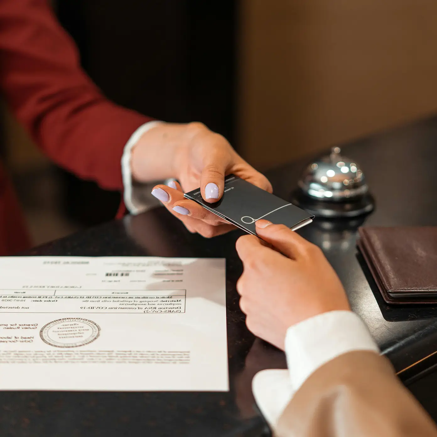 Close-up of a key card being handed across a counter beside paperwork and a service bell.