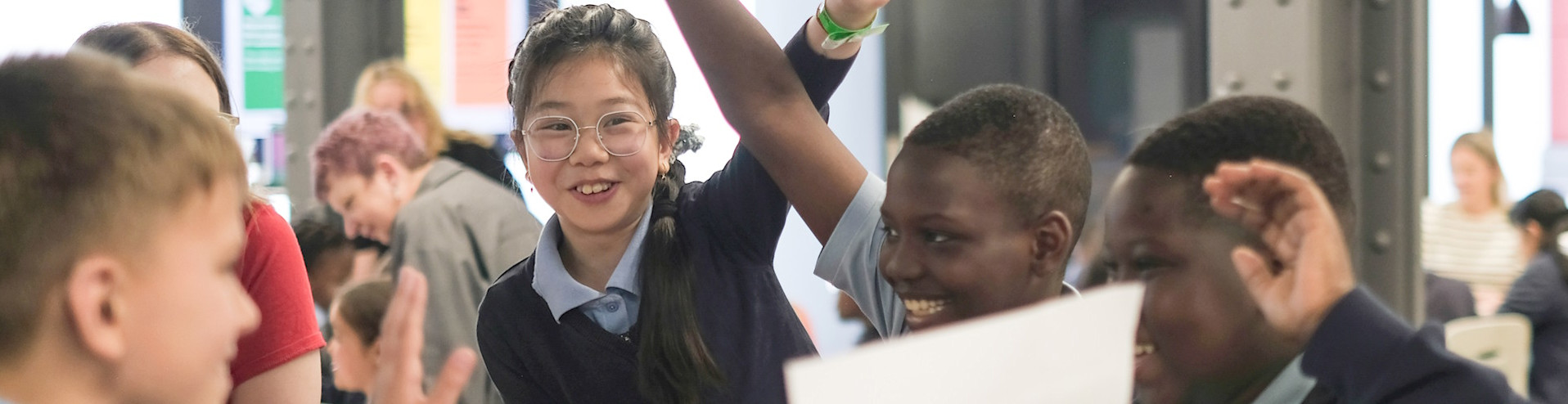 A group of kids raising their hands in the classroom, ready with task or answers