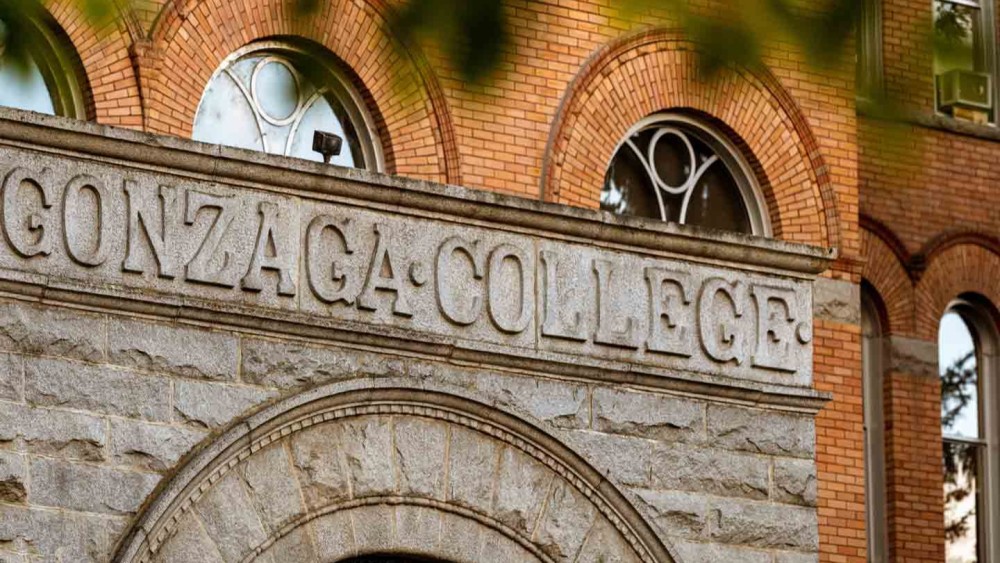 The exterior of a stone and brick building on Gonzaga University's campus is seen behind orange autumn leaves