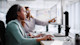 Two female international students enrolled in a professional course at their US university sit at a work station and collaborate on a work-study project in front of a monitor.