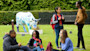 A group of international students at Heriot-Watt University in Edinburgh sit and stand on a lawn in front of a cow sculpture and have a conversation
