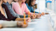 A row of students sit at a table holding pencils as they take a standardized test. 