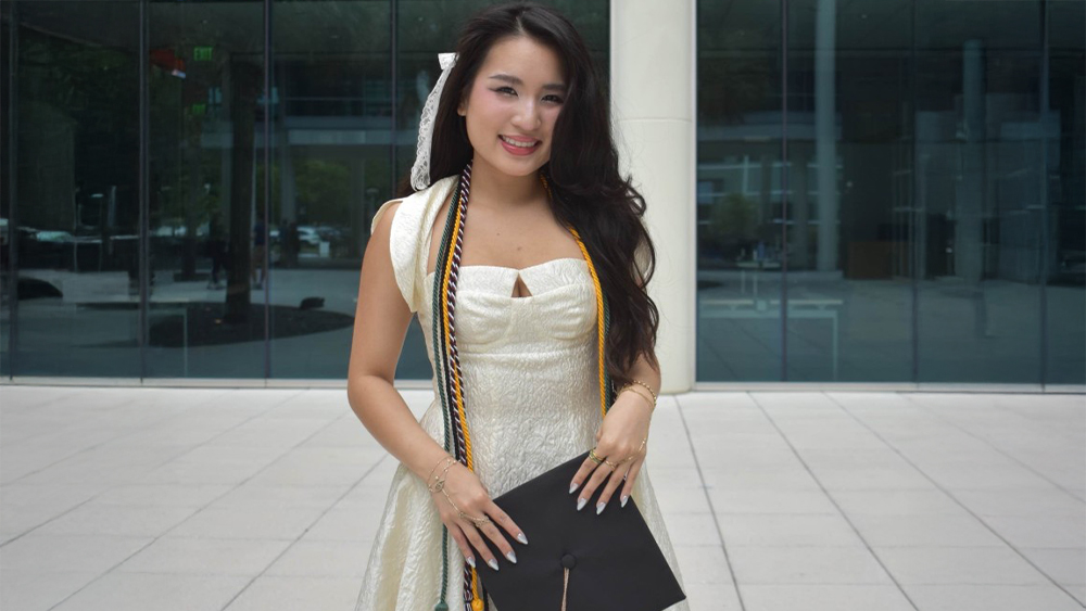 Jess, an international student from Vietnam at the University of South Carolina, stands with her graduation cap outside on campus after earning her supply chain management degree.