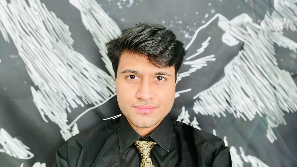 Abdullah, a computer science student from Pakistan at the University of the Pacific, stands in front of a chalkboard showing drawings of mountains and smiles for the camera