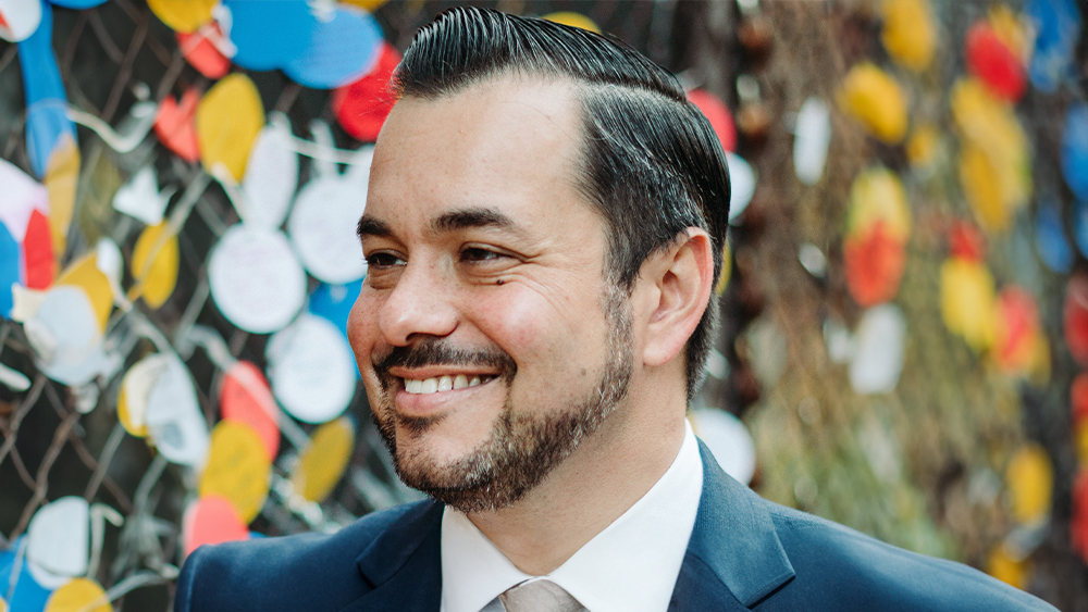 William Schaper, Adelphi International student services director at Adelphi University, stands in front of a colorful wall.