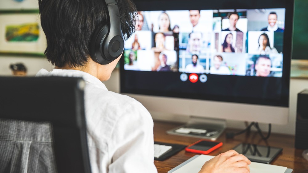 An international student wearing headphones sits across from a monitor to participate in a videoconference at his virtual externship program