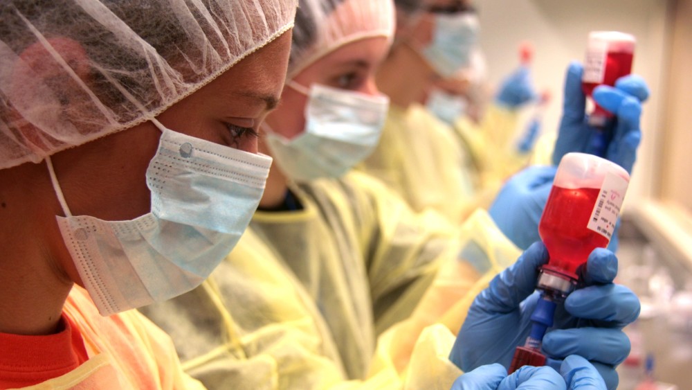 Three international students in the KU pharmacy program wearing PPE stand side by side in a lab