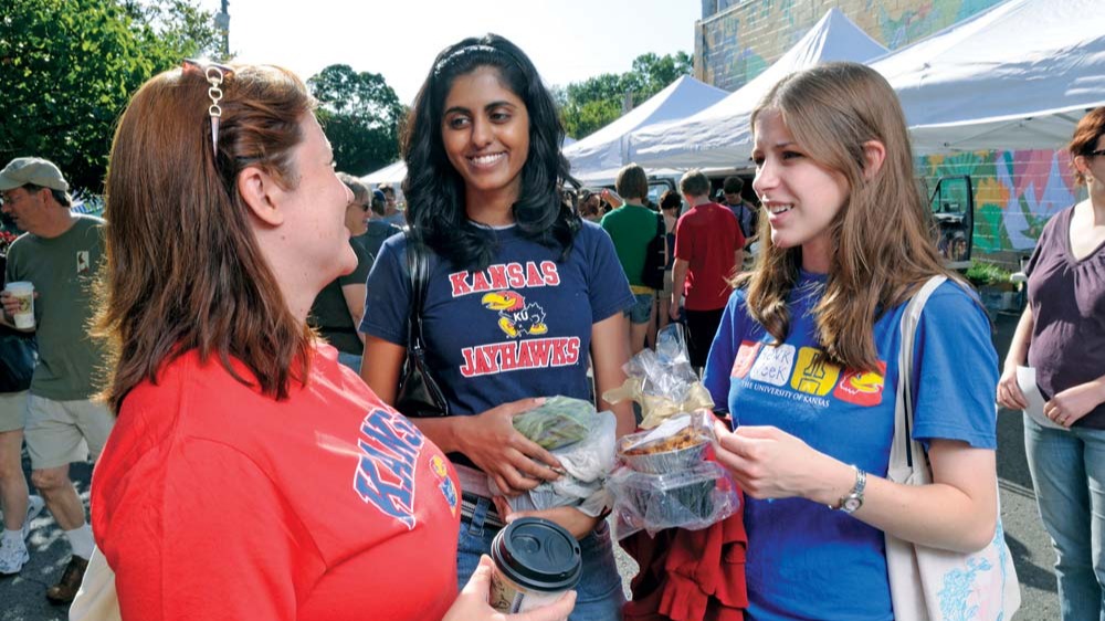 Three female Kansas students talk in a community outdoor market.