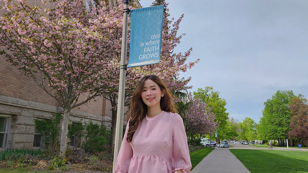 Gonzaga Global MBA student Daisy Le stands outside on campus in front of a flowering tree and green lawn and smiles for the camera