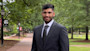 Mustafa, an international student from Saudi Arabia, stands in a suit and tie on the University of South Carolina campus and smiles for the camera. 