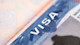 The top of a F-1 student visa is centered in the frame with white letters saying VISA on a blue background. Request an i 20 form from your US university to apply for your student visa.