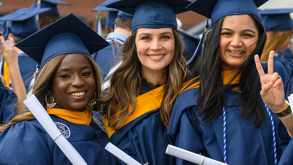 A group of female international students at Villanova University stand in their caps and gowns on graduation day and hold their new degrees. 